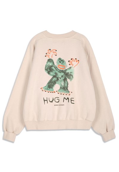 Sweat-shirt beige avec un monstre vert levant des mains oranges et le texte "HUG ME" et "BOBO CHOSES" au dos.