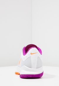 Sneakers Nike z białą siateczkową cholewką, purpurowymi akcentami i pomarańczowym logo. Teksturowana podeszwa w kolorze purpurowym z charakterystycznym wzorem.
