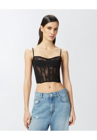 Crna kratka majica s čipkastim panelima, dekolteom u obliku srca i tankim naramenicama. Uparen s svijetloplavim iznošenim trapericama.