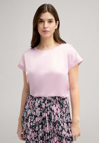 Lichtroze satijnen top met korte opgerolde mouwen, gecombineerd met een geplooide bloemenrok met een donkere achtergrond en roze bloemenpatronen.