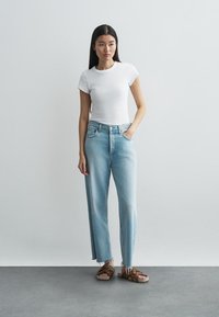 Ljusblå jeans med raka ben och hög midja, kombinerade med en vit figurnära t-shirt och bruna sandaler med nitar.