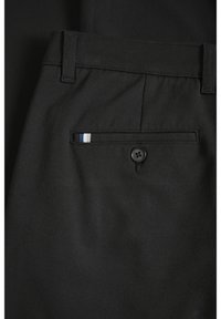 Svarta byxor har en passpojlomme med knappstängning, accentuerad av en liten blå, vit och blårandig detalj på lommens kant.