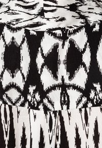 Czarna i biała tkanina z geometrycznym wzorem ikat, z kontrastującymi fakturami i charakterystycznymi kształtami w całym wzornictwie.