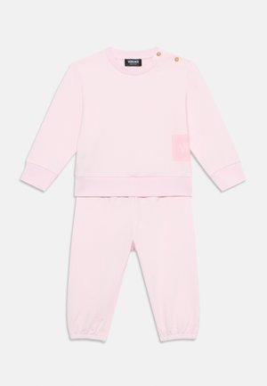 Różowy bawełniany sweatshirt i pasujące spodnie z ribbami. Zawiera guziki na ramionach oraz małą naszywkę z logo na klatce piersiowej.