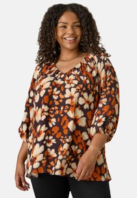 Blusa floreale in marrone scuro con motivi arancioni e crema; scollatura a V e maniche a palloncino; vestibilità ampia; tessuto leggero e testurizzato.