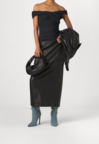 Off-shoulder musta ruched paita, mustat nahkahousut ja siniset nilkkasaappaat; pitää mustaa nahkalaukkua; sileät pinnat ja istuva muotoilu.