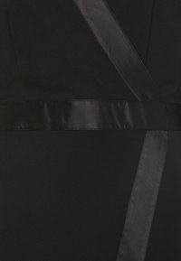 Robe noire avec une texture lisse et mate. Dotée d'une ceinture en satin noir brillant et de lignes diagonales de tissu créant un design structuré.