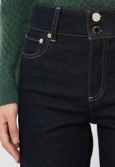 Dark blue denim jeans with five pockets, metal button, and gold stitching details. Close-up of waistband and upper leg area.
