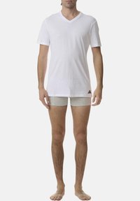 Biała bawełniana koszulka z dekoltem w serek oraz szare bokserki, z logo Adidasa, noszone przez męskiego modela stojącego boso.