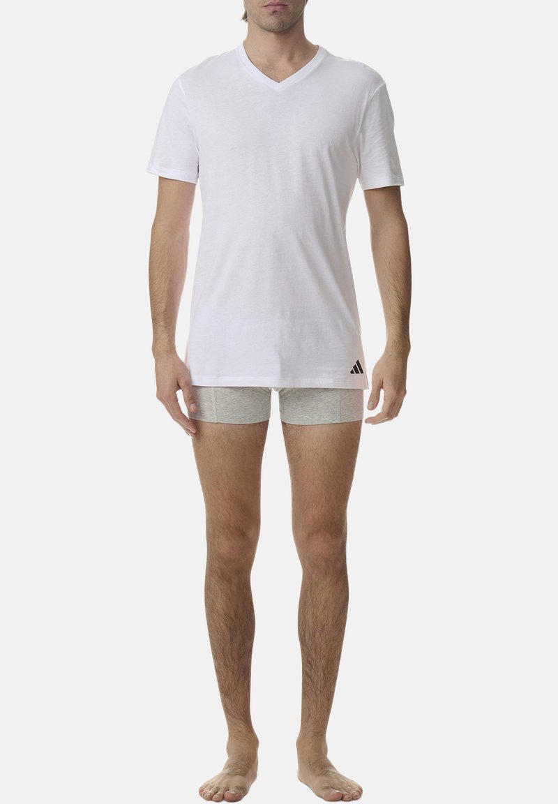 Biała bawełniana koszulka z dekoltem w serek oraz szare bokserki, z logo Adidasa, noszone przez męskiego modela stojącego boso.