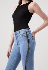 Un body negro con relieve y escote en forma de barco, combinado con unos jeans de tiro alto en azul claro que tienen una franja lateral negra de lentejuelas y bolsillos traseros.