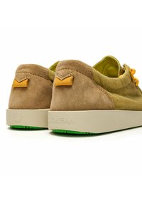 Scarpe in suede marrone con tomaia in tessuto testurizzato, dettagli gialli e suola in gomma beige con un motivo di battistrada verde.