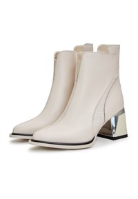 Bottes chevilles en cuir beige avec un bout pointu, des côtés côtelés et un talon bloc métallique. Comprend des surpiqûres de semelle noires contrastantes et des accents.
