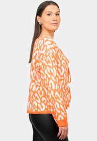 Maglione lavorato a maglia arancione con un motivo a stampa leopardata bianca, caratterizzato da una vestibilità ampia, maniche lunghe e lacci frontali. Tessuto testurizzato.