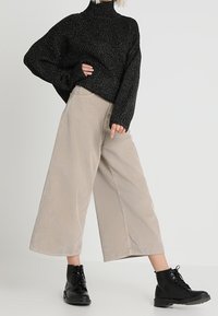 Black, sparkly oversized sweater with a high neckline, paired with beige, wide-leg corduroy pants and black lace-up boots.