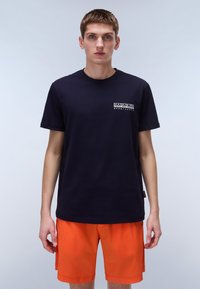 Camiseta de algodón azul marino con mangas cortas y un logotipo rectangular blanco en el pecho. Combinada con pantalones cortos de color naranja brillante.