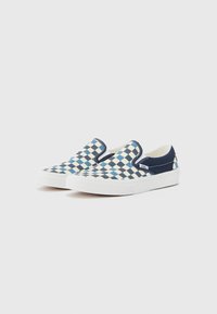 Zapatillas sin cordones con un patrón de tablero de ajedrez en azul marino y celeste, elaboradas en lona con una suela de goma blanca y detalles de costura.