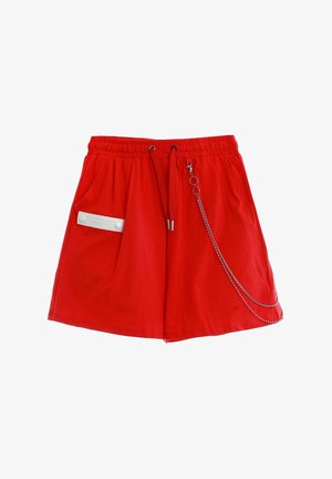 Pantalones cortos casuales de color rojo brillante con cintura elástica, cordón, bolsillo lateral con etiqueta blanca y cadena plateada decorativa colocada cerca de la cintura.