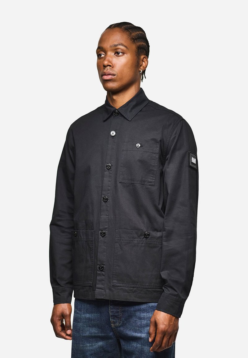 Schwarze Jacke mit Knopfverschluss und Kragen, ausgestattet mit einer aufgesetzten Tasche und zwei Fronttaschen. Hergestellt aus strukturiertem Stoff mit glänzenden Knöpfen.