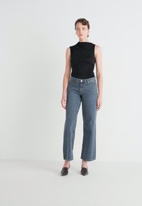 Black sleeveless top, fitted at the waist. Light blue high-waisted jeans, straight-leg cut. Brown pointed loafers, minimalistic design.