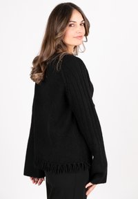 Black knitted sweater featuring ribbed texture, wide sleeves, and a fringed hem. Soft, cozy material designed for comfort.