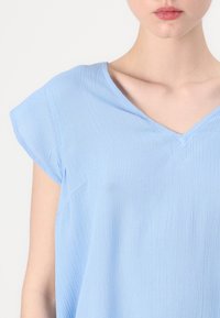 Blusa azzurro chiaro a maniche corte con scollo a V, realizzata in tessuto plissettato. Presenta una vestibilità comoda e una texture sottile.