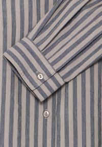 Camicia a righe in tessuto grigio chiaro e grigio scuro, caratterizzata da un polsino con bottoni e un unico bottone a perla, insieme a righe texturizzate.