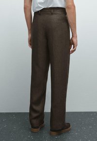 Brown, textured trousers with a loose fit, two back pockets, belt loops, and a plain finish. Worn with dark casual shoes.