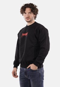 Felpa nera in misto cotone, design a girocollo, con un logo grafico rosso sul petto. Polsini e orlo a costine, vestibilità rilassata.