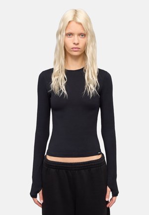 Zwart langmouwtop met een getailleerd ontwerp, ronde halslijn en zachte stof. Beschikt over verlengde manchetten en een cropped zoom. Gecombineerd met zwarte sweatpants.
