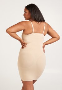 Nude bodycon-klänning med justerbara band, med slätt tyg och ribbad textur, designad för att följa kurvor.