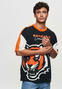 Lyhythihainen T-paita mustana, oranssina ja valkoisena, jossa on tiikeri graafinen kuva. "BENGALS Cincinnati" -teksti paksulla oranssilla fontilla. Puuvillamateriaali.