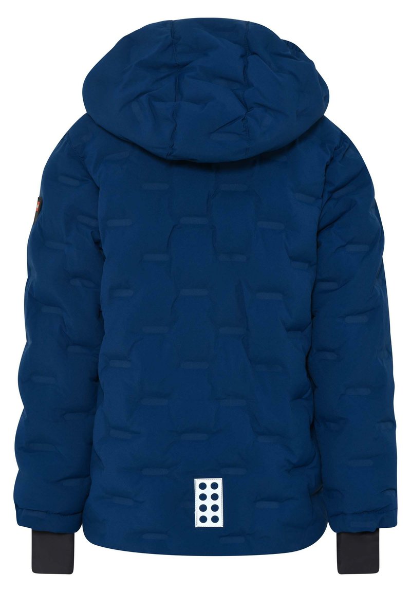 Veste en duvet bleu marine avec une capuche, design en matelassé texturé, poignets noirs, et une étiquette rectangulaire blanche avec des points noirs près de l'ourlet.
