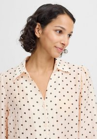 Light peach blouse with black polka dots, button-up design, classic collar, textured fabric, and slightly puffed sleeves.