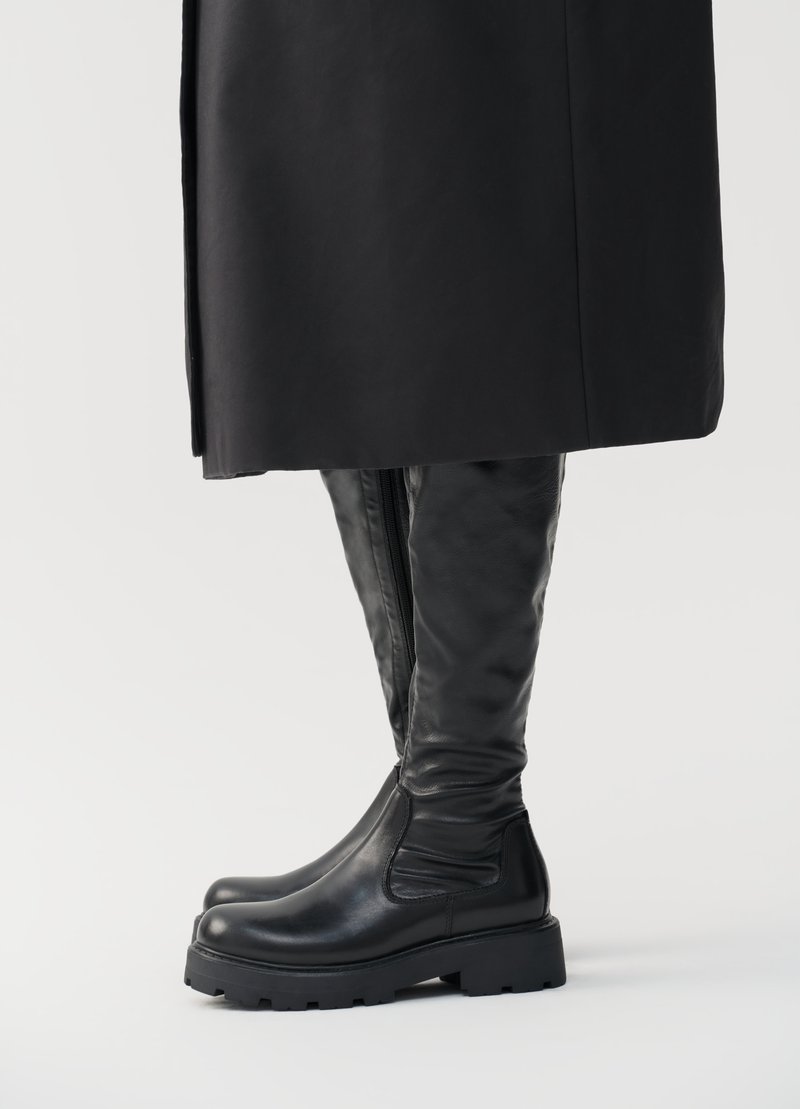 Bottes noires montantes en cuir lisse, avec une semelle épaisse et une fermeture éclair sur le côté pour un enfilage facile. Détails de coutures subtiles sur la tige.