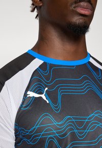 Zwart sportshirt met blauwe golfpatronen en witte meshpanelen, een blauwe kraag en een wit Puma-logo op de borst.