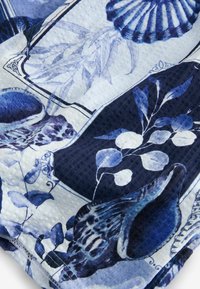 Tissu multicolore présentant un motif de coquillage et de feuille dans des nuances de bleu et de blanc, avec des éléments texturés et des motifs géométriques distincts.