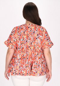 Blommig peplumtopp i orange och flerfärgade mönster, med korta volangärmar och en nyckelhålsdetalj bak. Tillverkad av lätt material.