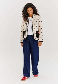 Krémová prešívaná bunda s čiernymi srdiečkovými vzormi, čiernymi vreckami a šnúrkami. Spárovaná s voľnými tmavými denimovými nohavicami a červenými teniskami.