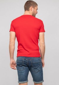 T-shirt rouge à manches courtes en coton, avec un design ajusté. Porté avec un short en denim à revers, affichant un style à cinq poches.