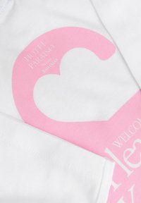 Άσπρο ύφασμα με ροζ γραφικό σχήμα καρδιάς και λευκό κείμενο που γράφει "HOTEL PARADISO" και "WELCOME".