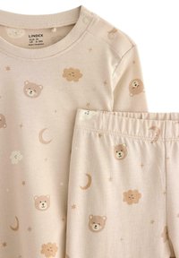 Mjuk bomullsoveralls-set för spädbarn i ljusbeige med mönster av björnar och moln. Inkluderar långärmad topp med tryckknappar och byxor med elastisk midja.