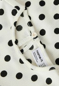 Witte stof met zwarte stippen, met een gestructureerd oppervlak, een ronde halslijn en een knoopdetail bij het label aan de binnenkant.