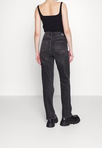 Vaqueros de mezclilla negros con pierna recta, cintura alta y bolsillos traseros. Llevados con una camiseta sin mangas negra y botas negras gruesas. Tejido texturizado.