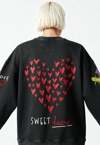 Čierna mikina s veľkým červeným srdcom, menšími srdciami a textom "SWEET heart" bielou farbou, spolu s kvetinovými akcentmi na rukávoch.