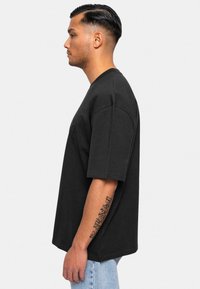 Camiseta oversized negra de algodón, con mangas cortas y escote redondo. Corte ligeramente suelto sin logotipos ni patrones visibles.