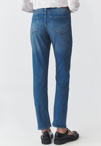 Vaqueros de mezclilla azul con un corte ajustado, que cuentan con dos bolsillos traseros y una cinturilla clásica. Combinados con zapatos de charol negros y pernera recta.