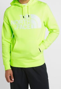 Ljus neongrön hoodie gjord av mjukt tyg, med en stor vit logotyp, justerbar dragsko på huvan och framficka.