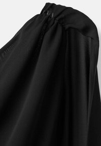 Tela negra con una textura suave y liviana, con detalles de hombros fruncidos. La prenda cae de manera elegante, realzando el movimiento fluido.