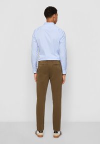 Camisa a rayas azul claro de manga larga, combinada con pantalones chinos marrones. La camisa tiene un cuello estándar y los chinos presentan un diseño limpio.